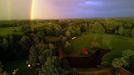 Eine-Umgekehrte-Aufnahme-Eines-Leuchtenden-Regenbogens-In-Einer-Grünen-Landschaft-Mit-Einem-Wald-Und-Einem-Kleinen-Viertel