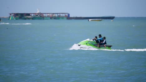 A-man-with-two-children-with-lifejackets-riding-the-green-Jet-Ski-speeding-to-the-left-in-Pattaya,-Thailand