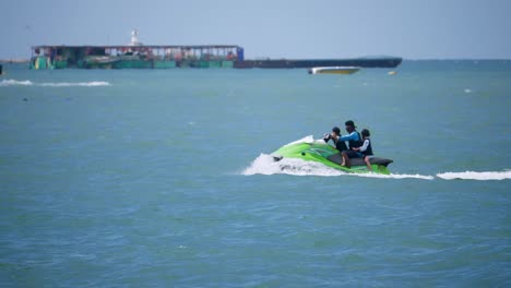 Un-Hombre-Con-Dos-Niños-Con-Chalecos-Salvavidas-Montando-La-Moto-Acuática-Verde-Acelerando-Hacia-La-Izquierda-En-Pattaya,-Tailandia