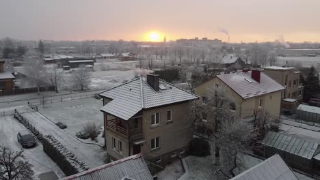 Cinematic-aerial-view-of-the-scenic-European-town-in-snow-at-sunrise,-Winter-landscape-house-and-sunrise-in-the-background