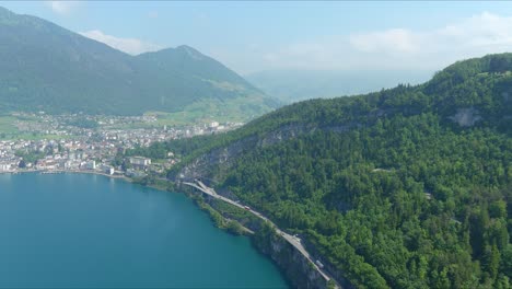 Morschach-Flyover:-Moving-Over-Scenic-Water-Valley-Towards-Alps-Mountains,-Switzerland,-Europe,-Drone-|-Closer-Inland-Movement-Along-Road-Cliffside-Beside-Majestic-Blue-Lake