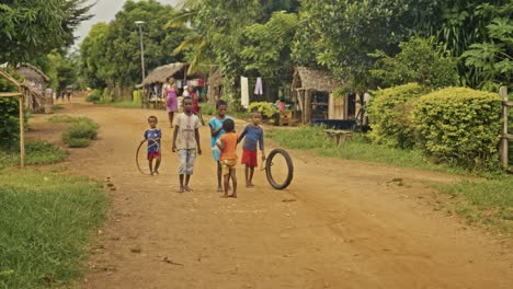 Arme-Afrikanische-Kinder-Stehen-Mit-Fahrradrädern-Als-Spielzeug-Auf-Einer-Staubigen-Straße-Im-Dorf