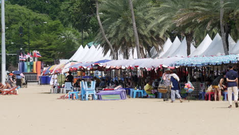 Verkäufer,-Menschen,-Die-Den-Strand-Genießen,-Liegestühle,-Sonnenschirme-Und-Vordächer,-Belebtes-Strandszenario-In-Pattaya,-Thailand