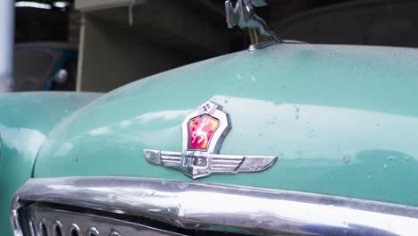 Light-blue-green-bonnet-and-chrome-front-grille-of-the-historic-Volga-M21-with-red-emblem-and-a-statue-with-a-rearing-stag