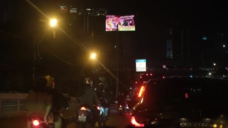Motorräder-Fuhren-Während-Einer-Roten-Ampel-Weiter,-Während-Große-Fahrzeuge-Anhielten,-Die-Überführung-Bewegt-Sich-Nach-Rechts,-Während-Große-LED-Werbetafeln-Mit-Autowerbung-übersät-Sind,-Bangkok,-Thailand