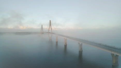 Rising-aerial-view-of-Replot-Bridge,-Finland,-on-misty-morning