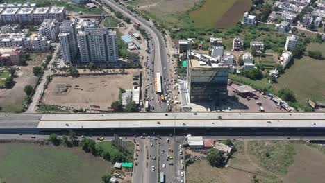 Cámara-De-Drones-Con-Vista-Aérea-De-La-Ciudad-De-Rajkot-Bajando-Donde-Hay-Mucho-Tráfico-Al-Lado-Del-Complejo-Y-Muchas-Bicicletas-Y-Camiones-De-Cuatro-Ruedas-Estacionados-En-El-Estacionamiento