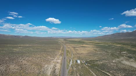 Long-Flat-Road-in-Nevada-high-desert---aerial-flyover-with-blue-sky-and-white-clouds