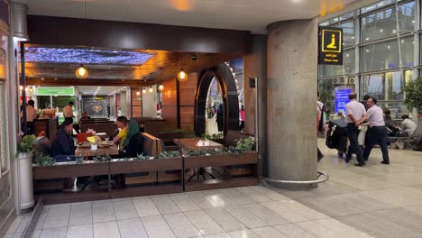 Café-Lounge-Flughafen-Im-Iran-Teheran-Ika-Khomeini-Flugplatz-Vor-Der-Passkontrolle-Flugtafel-Zeigt-Den-Flugplan-Und-Wartende-Menschen,-Die-Zeit-In-Der-Halle-Verbracht-Haben-Reisende,-Die-Eine-Reise-Zum-Iranischen-Wahrzeichen-Haben