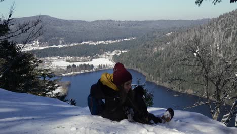 A-young-woman-lays-on-the-snow-to-relax-after-reaching-the-viewpoint-over-Lake-Longemer-in-the-Vosges-Mountains