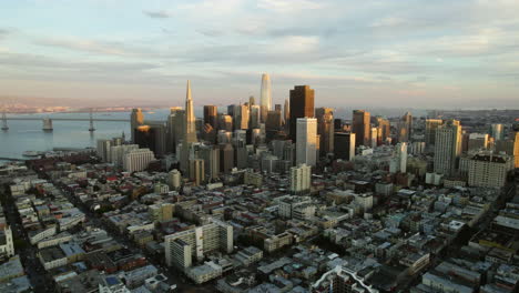 Aerial-view-rising-in-front-of-sunlit-skyline-of-San-Francisco,-golden-hour-in-USA