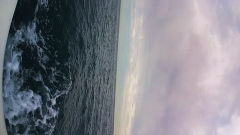 Sailing-in-open-deep-sea-with-moody-cloudscape-above,-vertical-view
