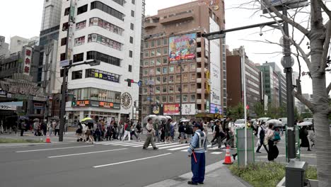 Gente-Cruzando-La-Avenida-Midosuji-En-Dotonbori-Con-Algunos-Sosteniendo-Paraguas-En-Un-Día-Nublado