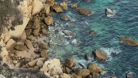 Waves-rolling-into-a-rocky-coastline-with-beautiful,-turquoise-water-as-seen-from-above