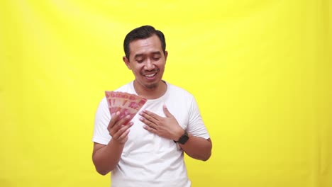 Relieved-asian-adult-man-holding-Indonesia-banknotes-while-touching-his-chest