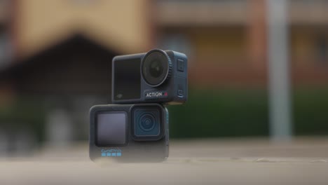 Cámara-Dji-Osmo-Action-4-Apilada-Encima-De-Gopro-Hero-12-Sobre-Una-Mesa-Con-Fondo-Bokeh