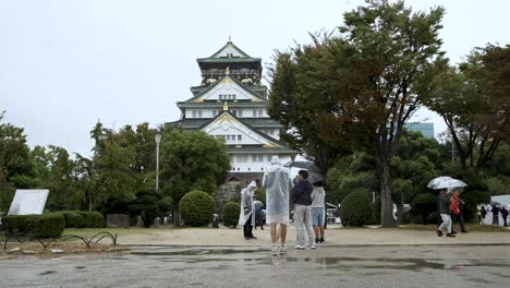 Touristen,-Die-Regenponchos-Tragen,-Fotografieren-Die-Burg-Von-Osaka-An-Einem-Regnerischen,-Bewölkten-Tag-In-Osaka