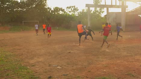 Children-and-young-men-playing-football-on-a-dusty-community-pitch-in-Kumasi-during-the-afternoon,-Ghana