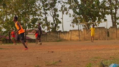 Goalkeeper-in-yellow-jersey-kicks-the-ball-away-to-the-opposite-side-after-stopping-a-freekick,-community-soccer-field,-Kumasi,-Ghana