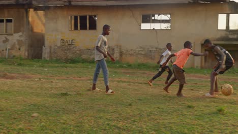 Proud-boy-in-an-orange-shirt-dribbling-the-ball-bare-feet-going-through-a-lot-of-players-then-goes-towards-the-camera-smiling-with-joy,-community-football-pitch,-Kumasi,-Ghana