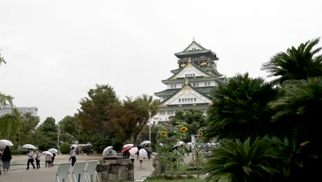 Visitantes-Con-Sombrillas-Caminando-Hacia-El-Castillo-De-Osaka-En-Un-Día-Lluvioso-Y-Nublado