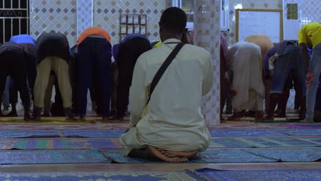 Solo-man-rubs-eye-after-bowing-to-return-to-kneeling-position-in-mosque,-rearview