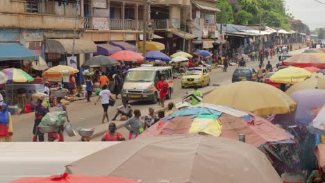 Medium-static-of-old-van-and-taxi-driving-in-Adum-market-with-vendors-under-umbrellas