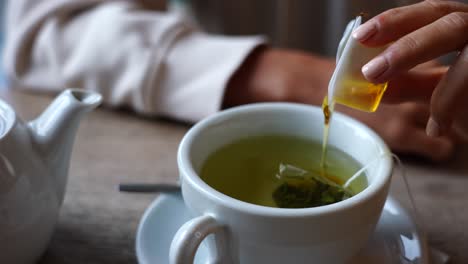 Close-up-of-girl-hand-hold-small-plastic-honey-cup-and-add-it-to-green-tea
