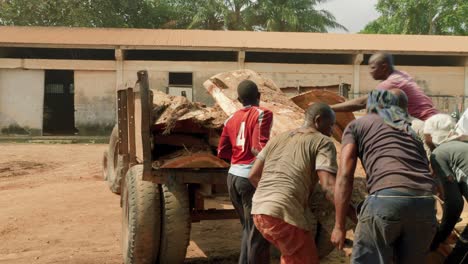 Group-of-African-men-work-together-to-lift-large-roughly-machined-log-into-back-of-work-truck-in-dusty-dry-environment