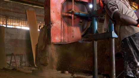 Workers-lean-against-sawmill-pushing-to-guide-it-as-sawdust-spills-out-in-slow-motion