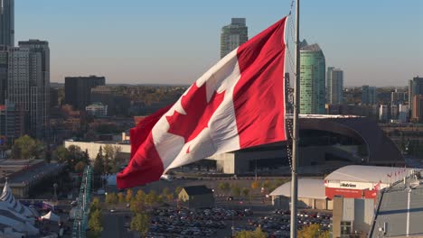 A-closeup-drone-view-of-a-Canadian-flag-near-the-Calgary-stampede-grounds,-BMO-center-and-Scotiabank-center-home-to-the-Calgary-Flames