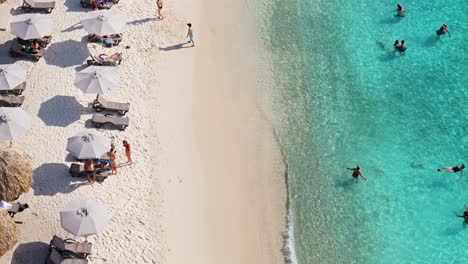Athletic-men-and-woman-tourists-swim-in-crystal-clear-blue-water-and-walk-on-beach-of-Grote-Knip-Curacao