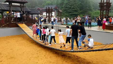 Grupo-De-Gente-Asiática-Hombre-Mujer-Niño-Niña-Jugando-Balanceándose-En-Un-Puente-Colgante-Colgante-De-Madera-En-El-Patio-De-Recreo-En-China---Parque-Temático-Chino