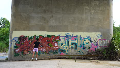 Slow-motion-shot-of-a-man-spray-painting-graffiti-onto-a-bridge-pillar