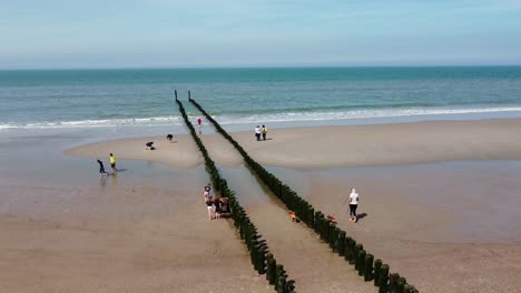Long-groyne-reaching-into-the-sea-surrounded-by-a-few-people-at-a-beach-in-the-Netherlands