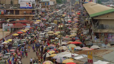 Throngs-of-people-crowd-walking-on-dirt-street-lined-with-umbrellas-and-vendor-stalls-at-Adum-market