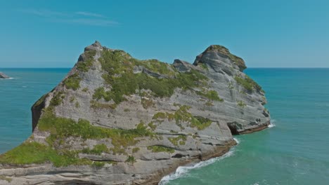 Aerial-drone-flight-over-wild,-rugged-and-rocky-outcrop-landscape-in-the-Tasman-Sea-at-popular-tourist-destination-of-Cape-Farewell,-South-Island-of-New-Zealand-Aotearoa