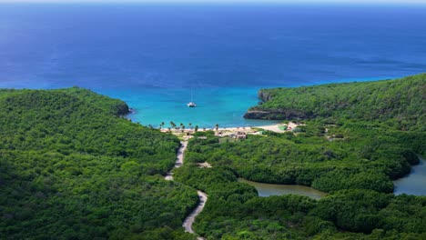 Drone-dolly-above-winding-road-leading-to-Santa-Cruz-beach,-Curacao