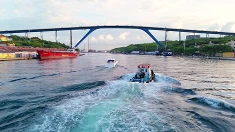 Rearview-aerial-follows-boats-driving-up-under-bridge-in-Willemstad-Curacao