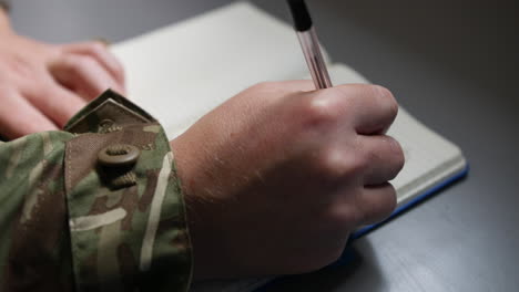 Unrecognizable-army-soldier-marine-writing-in-a-book-or-diary-with-a-pen-close-up-on-hand