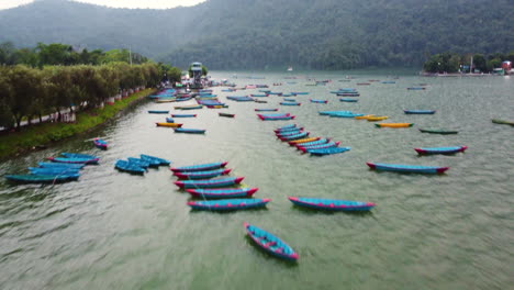 Canoas-De-Color-Azul-Y-Naranja-Brillantes-Ancladas-Y-Atadas-En-Un-Lago-Cerca-De-Pokhara,-Nepal
