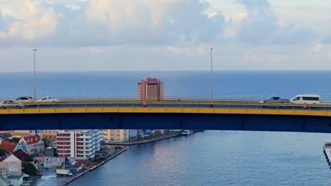Drone-rises-to-reveal-iconic-colorful-buildings-of-Willemstad-Curacao-passing-traffic-driving-on-bridge