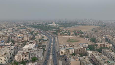 Aerial-drone-shot-over-cricket-playgrounds-and-buildings-alongside-MA-jinnah-Road,-Karachi,-Pakistan-on-a-cloudy-day
