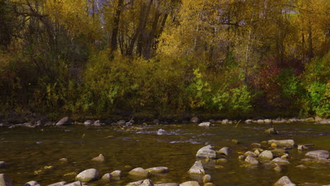 Fluss-Fließt-Durch-Felsen-Mit-Herbstbäumen-Im-Hintergrund