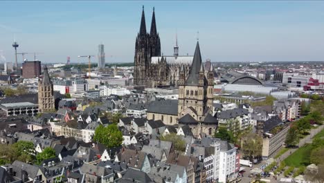 Towering-steeple-spires-of-cologne-Cathedral-and-city-hall-above-rooftops,-Aerial