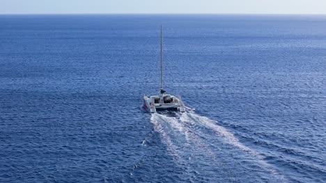 Rear-view-drone-descends-as-catamaran-drives-to-open-ocean-on-Caribbean-coastline-of-Westpunt,-Curacao