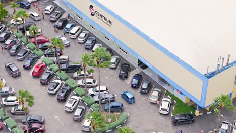 Luftumlaufbahn-Um-Einen-Tropischen-Supermarkt,-Während-Autos-Kreisen,-Um-Einen-Parkplatz-Zu-Finden