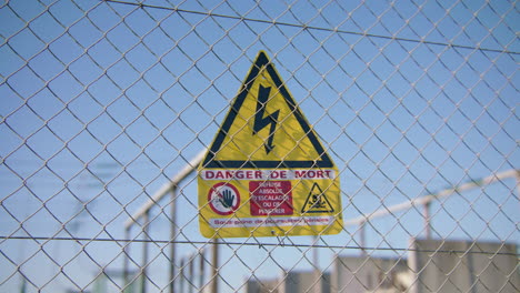 Gelbes-Schild-Mit-Der-Gefahr-Eines-Stromschlags,-Das-Auf-Einem-Hohen-Zaun-Angebracht-Ist