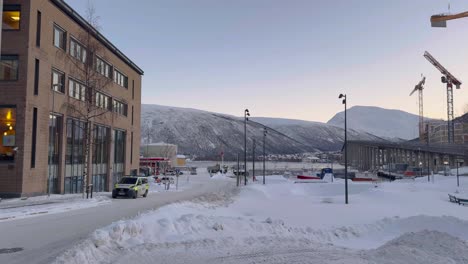 Toma-Panorámica-De-Edificios-Cubiertos-De-Nieve-Y-Tráfico-En-Tromso,-Noruega,-Con-Grúas-De-Construcción-En-La-Distancia.