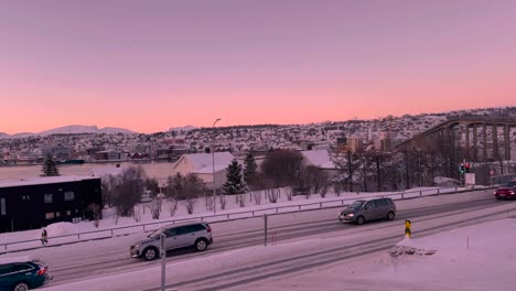 Panning-shot-of-bridge-and-snow-covered-roads-in-Tromso-Norway,-with-water-and-mountains-in-the-distance